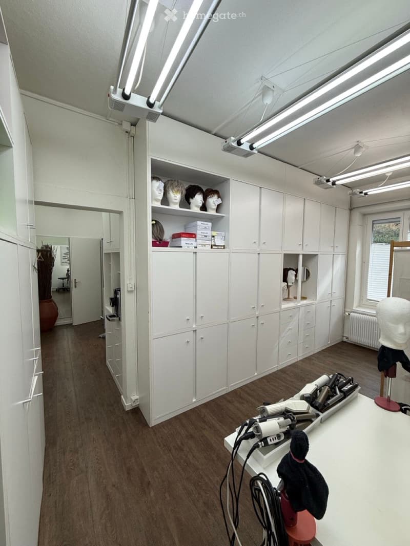 A well-lit salon or styling room with white cabinets, a large mirror, a white table with hair styling tools, mannequin heads, and storage boxes.