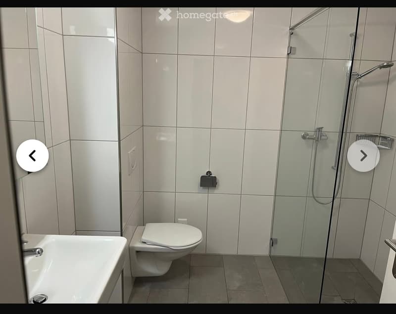 Modern bathroom with white tiled walls, a bathtub, toilet, and a glass-enclosed shower area.