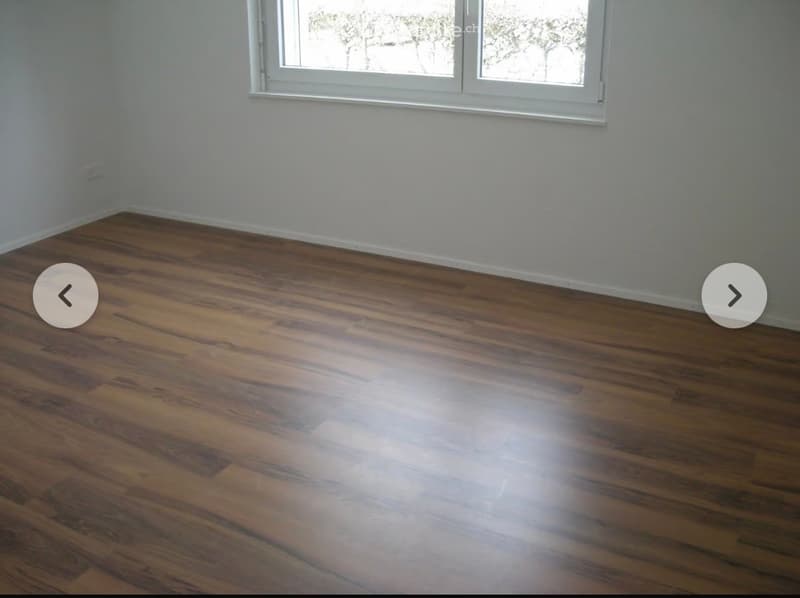 Empty room with wooden flooring and white walls, featuring a large window with white frames.
