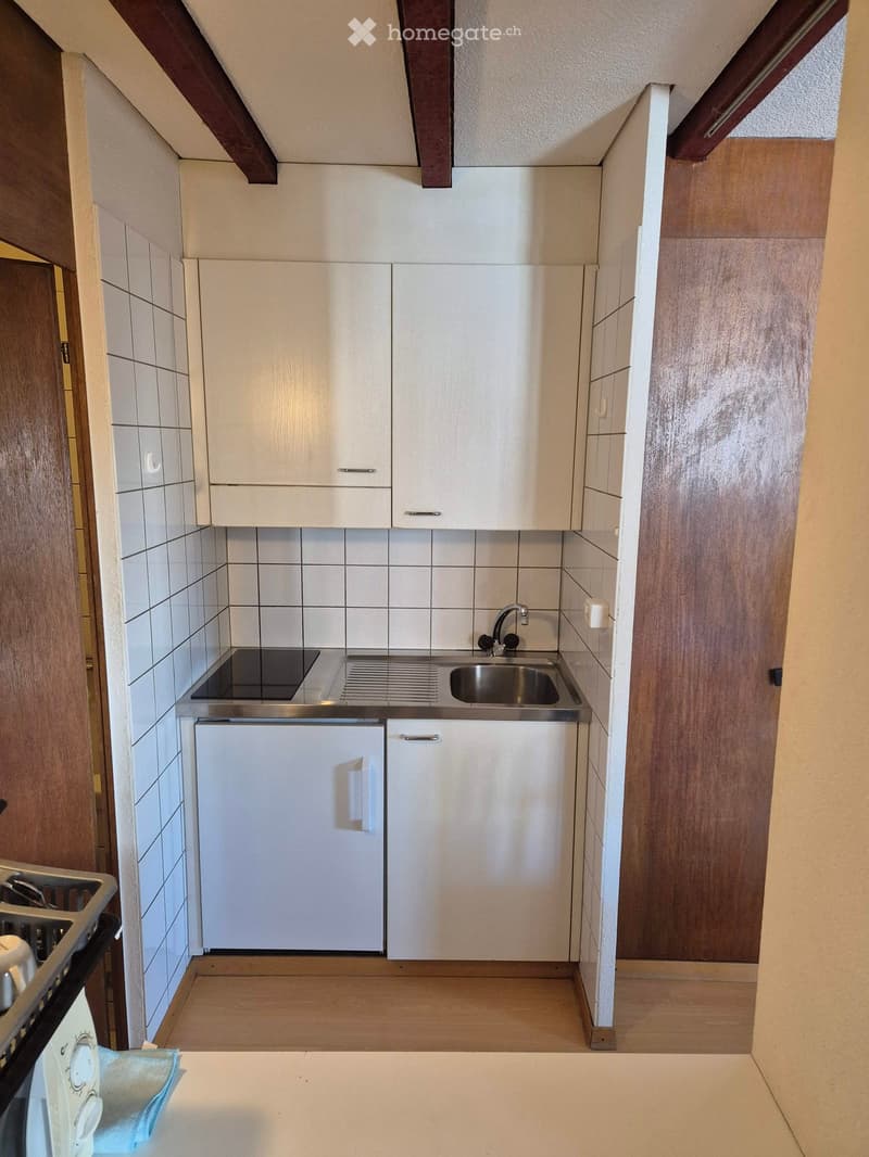 Modern kitchen with white cabinets, stainless steel sink, and appliances including a refrigerator, oven, and microwave. The space features wooden flooring and tiled backsplash.