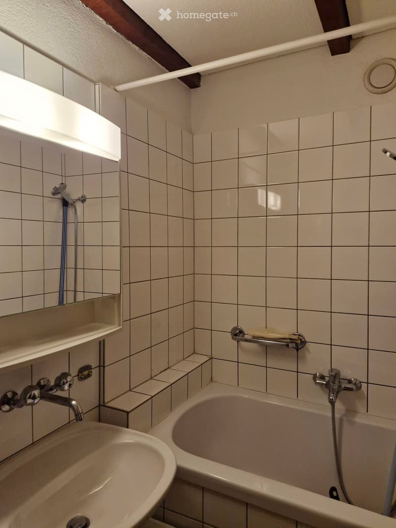 Bathroom with tiled walls and floor, featuring a bathtub, sink, mirror, and towel rack.