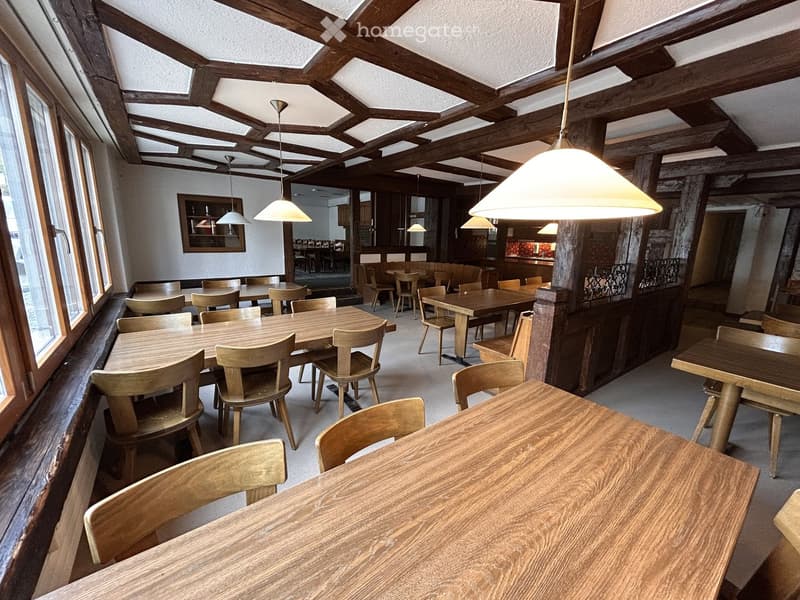 Restaurant or dining area with wooden tables and chairs, exposed wooden beams, pendant lights, and large windows.