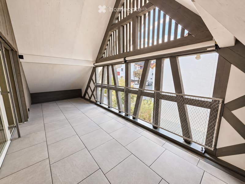 Modern balcony with tiled floor, wooden beams, and metal railing, offering a view of the surrounding area.