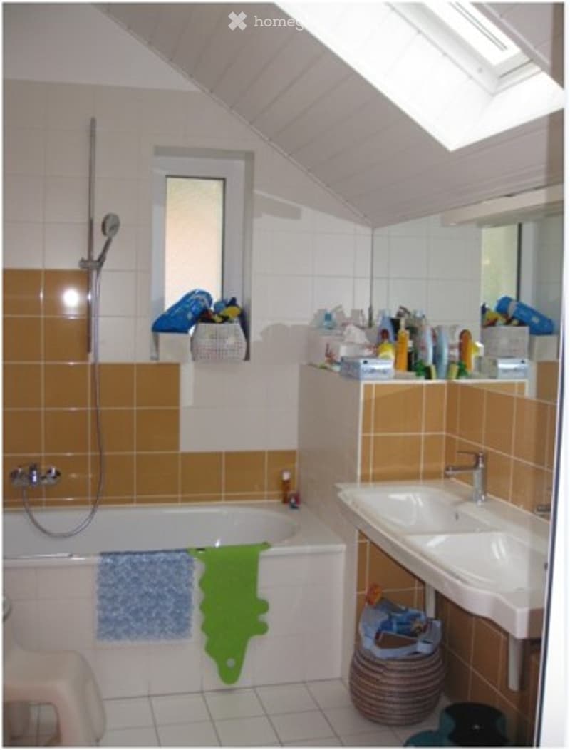 Bathroom with a bathtub, shower, sink, and mirror. The walls are tiled in orange and white, and there are towels and storage baskets visible.