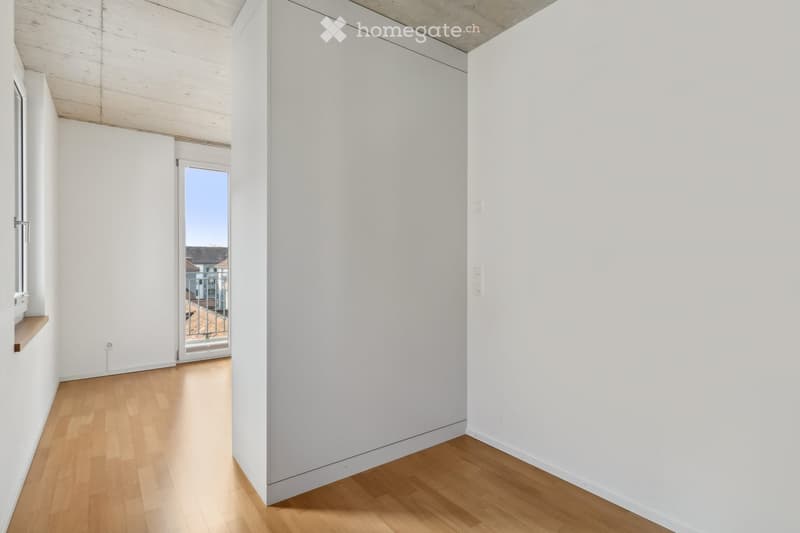 Empty room with white walls, wooden flooring, and a sliding glass door leading to a balcony or outdoor area.