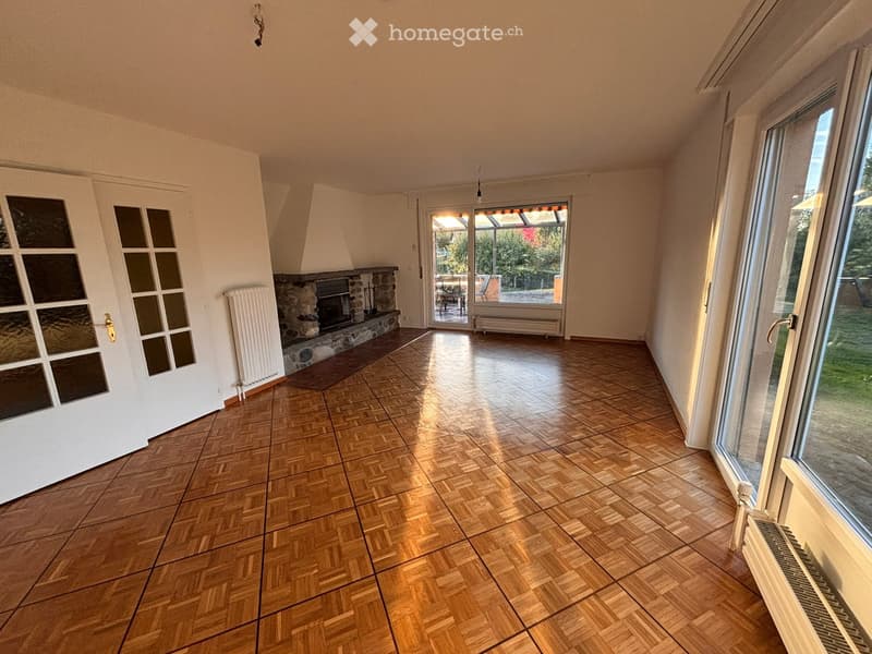 Empty room with wooden parquet flooring, white walls, fireplace, large windows, and a door leading to a balcony or terrace.