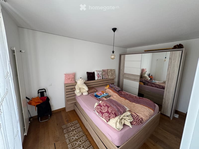 A cozy bedroom with a wooden bed, colorful bedding, a large mirror, a wardrobe, and a small stool with a teddy bear on top.