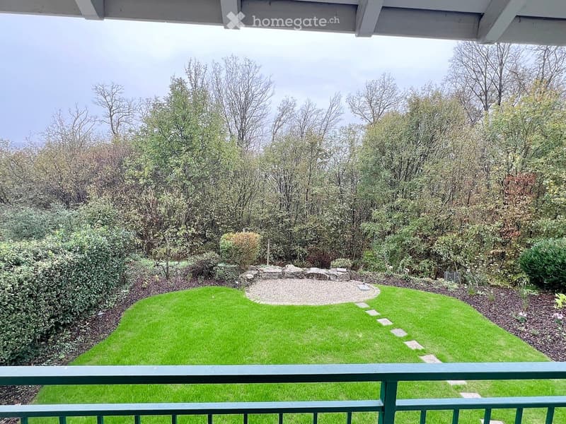 Balcony overlooking a well-maintained lawn with a stone pathway leading to a circular gravel area surrounded by trees and shrubs.