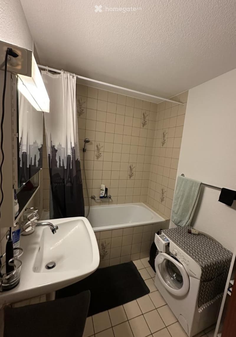 Bathroom with a sink, bathtub, shower curtain, mirror, and a washing machine in the corner.