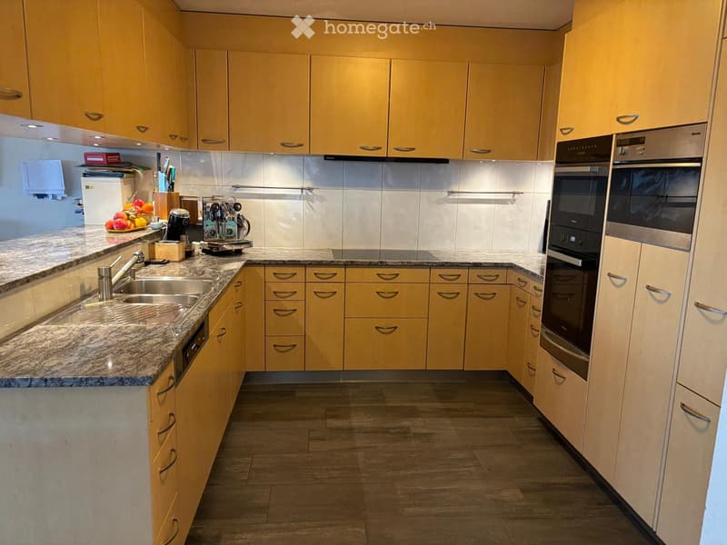 Modern kitchen with light yellow cabinets, granite countertops, stainless steel appliances, and a fruit bowl on the counter.