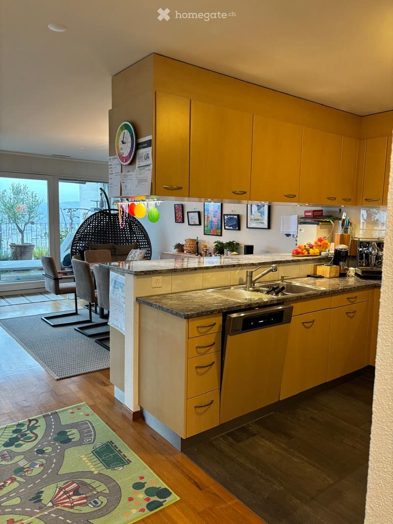 Bright kitchen with yellow cabinets, granite countertop, sink, dishwasher, and various appliances. A small seating area with chairs and a table is visible, along with a colorful rug and balloons hanging from the ceiling.