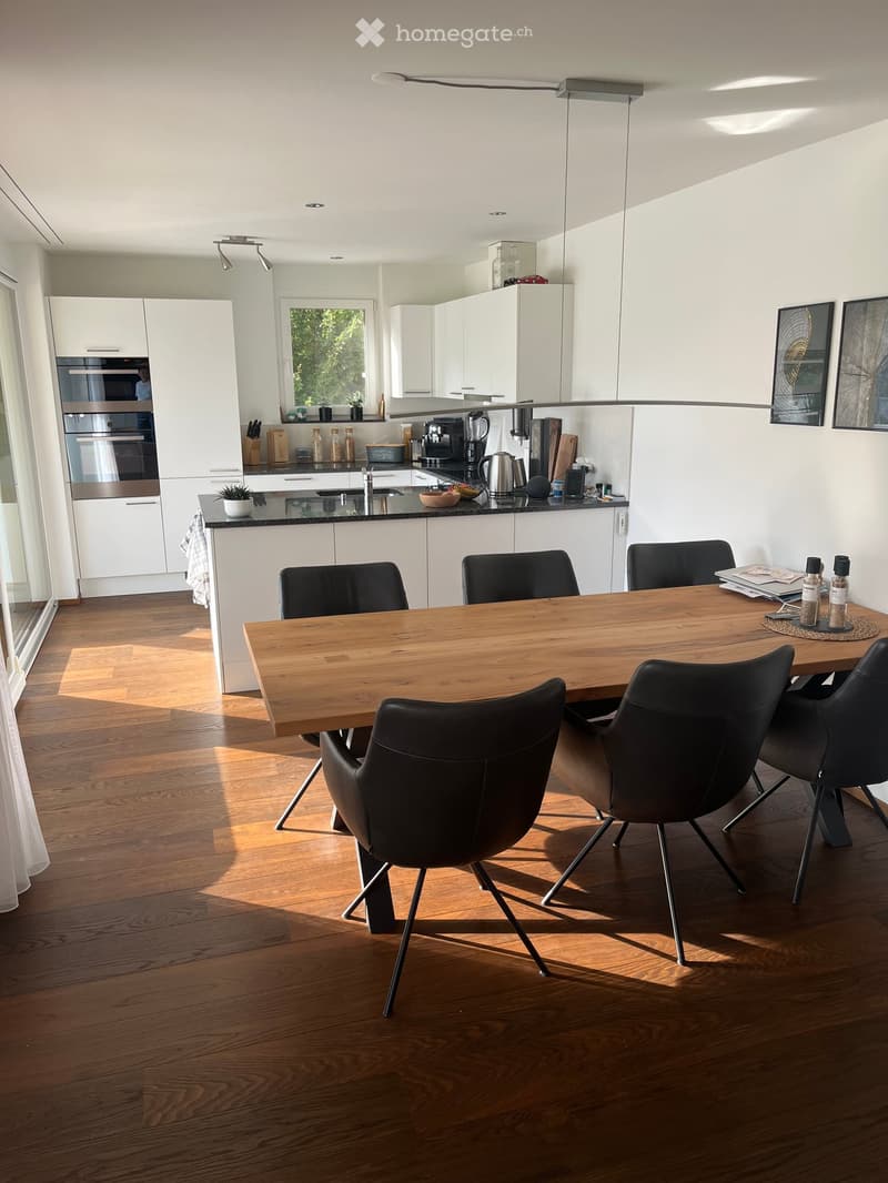 Modern kitchen with white cabinets, dark countertops, a wooden dining table with black chairs, and various appliances including an oven and refrigerator.