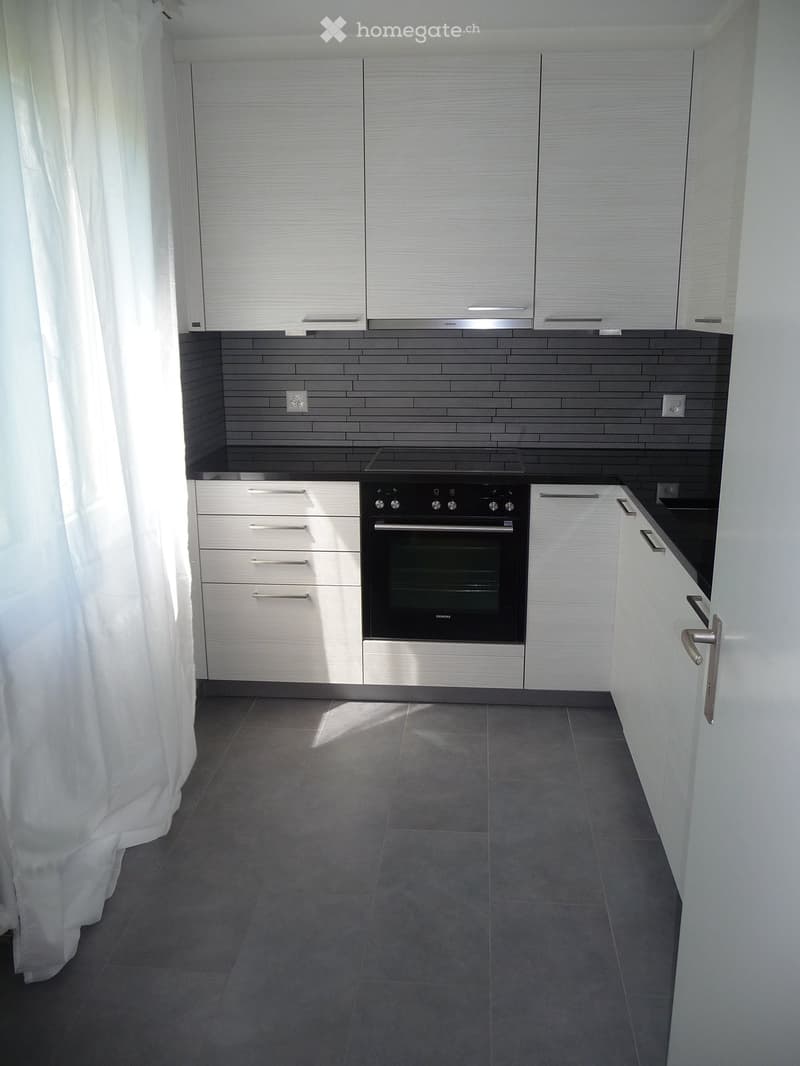 Modern kitchen with white cabinets, stainless steel oven, dark tiled backsplash, and grey tiled floor.