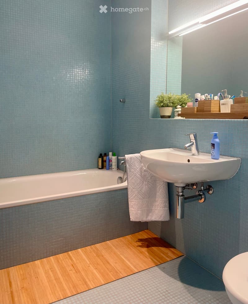 Bathroom with blue tiled walls, a white bathtub, a sink with a modern faucet, a towel, and a small plant on a shelf.