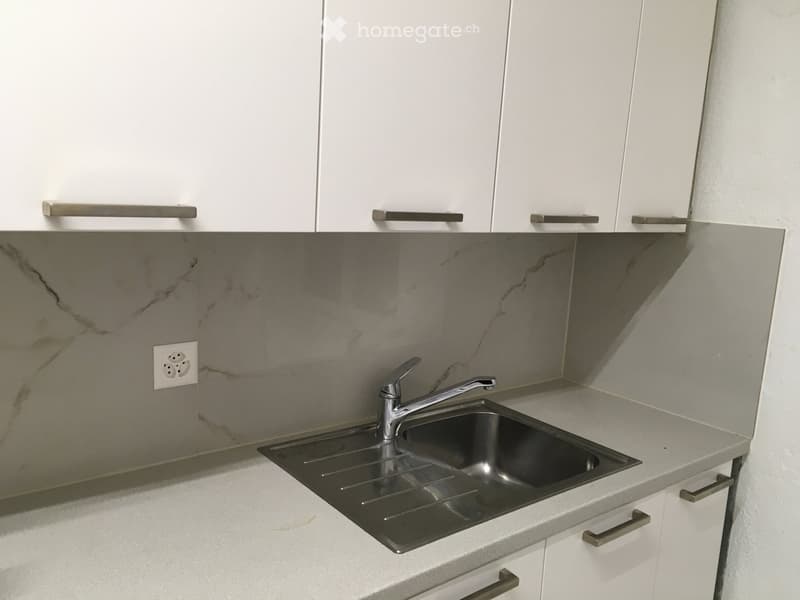 Modern kitchen with white cabinets, marble backsplash, and stainless steel sink.