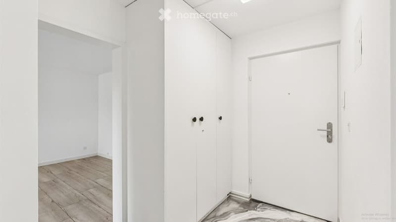 Empty room with white walls, wooden flooring, and a closed white door.