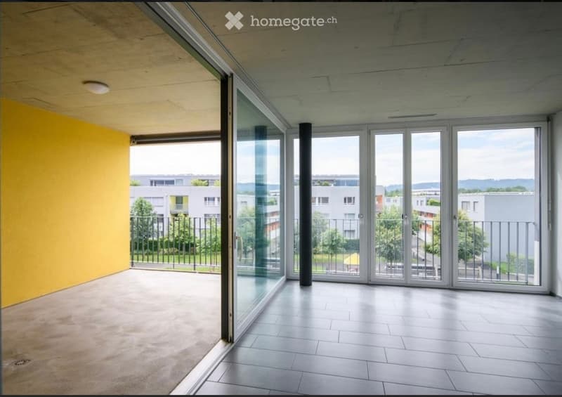 Empty balcony with large glass doors, tiled floor, yellow wall, and metal railing overlooking a residential area.