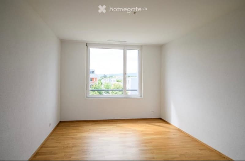 Empty room with wooden flooring, white walls, and a large window offering a view of the outside.