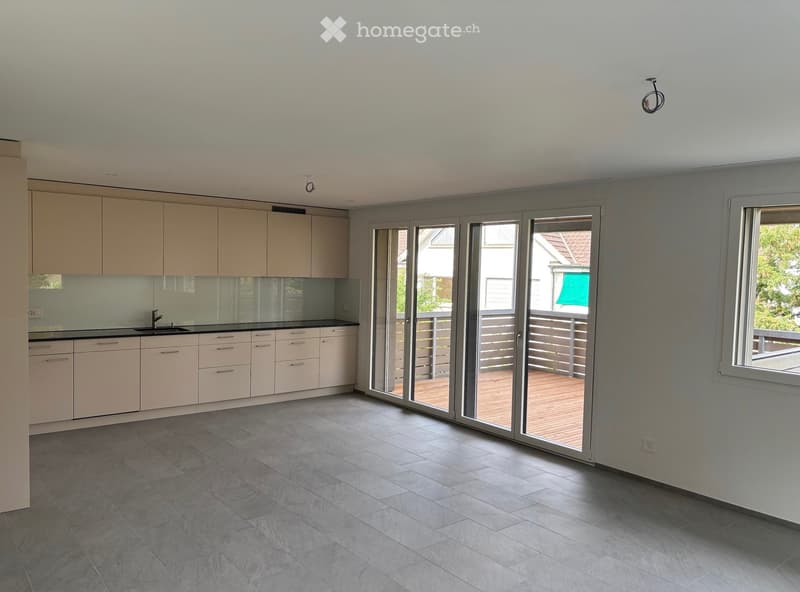 Empty kitchen with light-colored cabinets, a sink, and large sliding glass doors leading to a balcony.