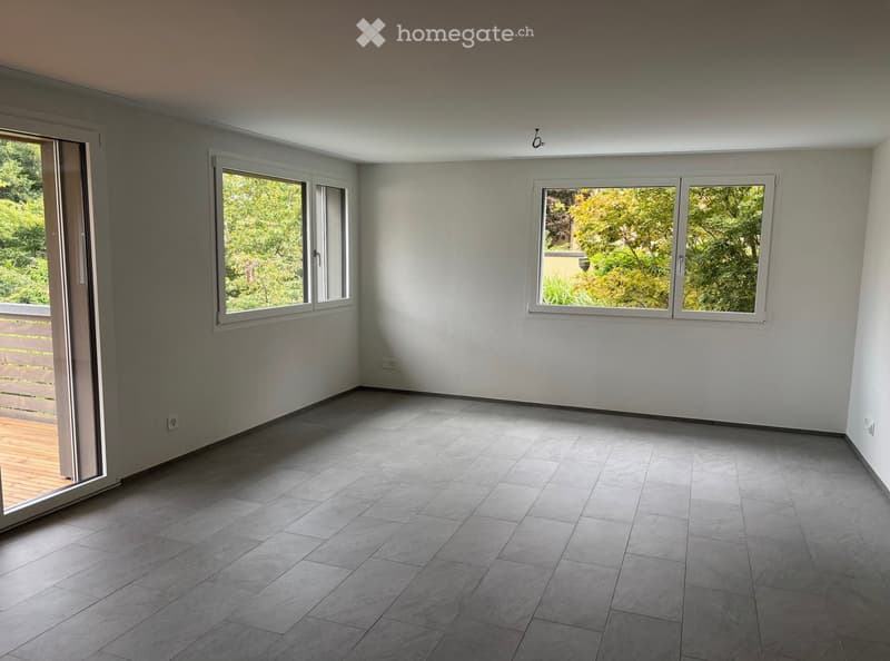Empty room with grey tiled floor, white walls, large windows, and a sliding glass door leading to a wooden deck.