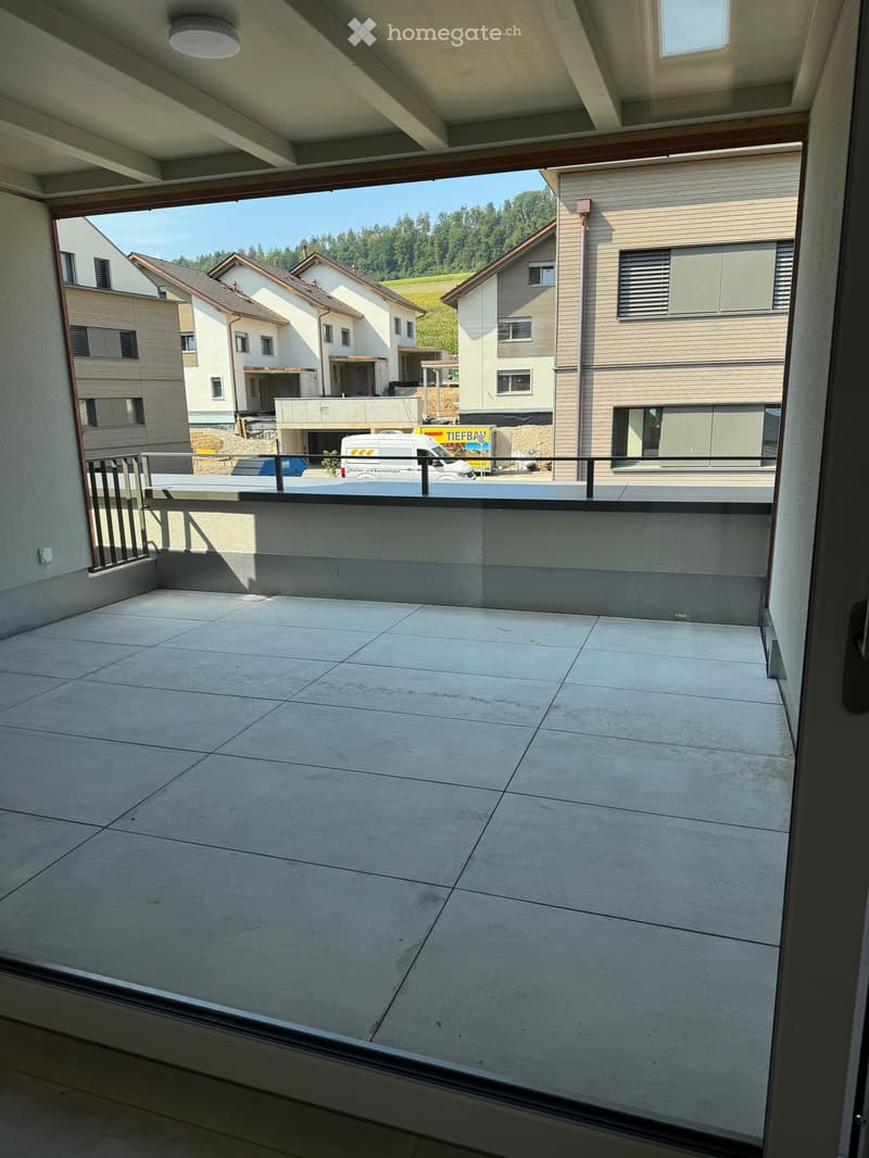 Balcony with tiled floor, glass railing, and view of neighboring houses and greenery.