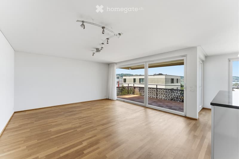 Empty room with wooden flooring, white walls, large sliding glass doors leading to a balcony, and modern lighting fixtures.