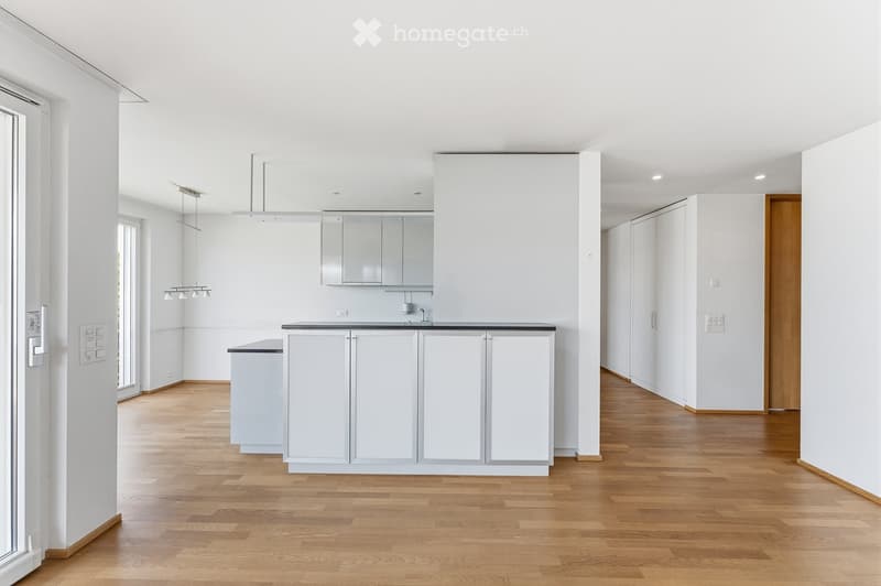 Empty kitchen area with white cabinets, a central island, and wooden flooring. No furniture or appliances are present.