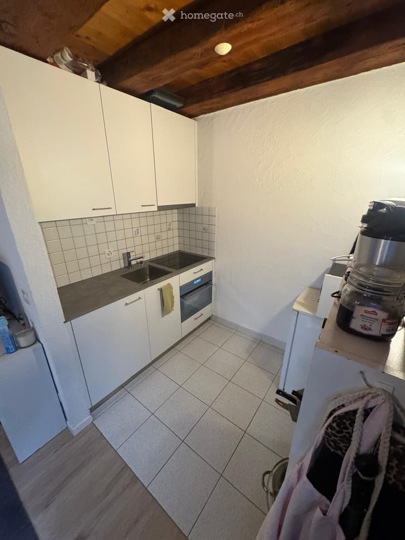 Modern kitchen with white cabinets, tiled backsplash, stainless steel sink, and built-in oven. Includes a countertop with a jar and a bottle.