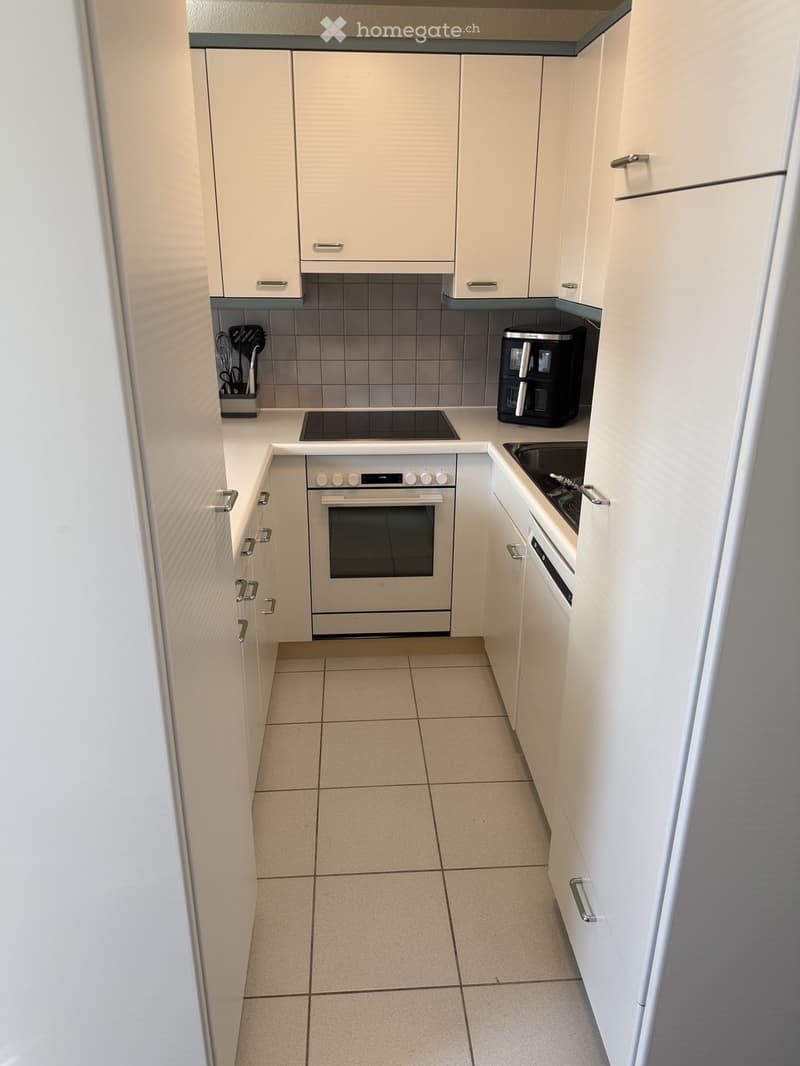 Modern kitchen with white cabinets, tiled floor, oven, sink, and coffee maker.