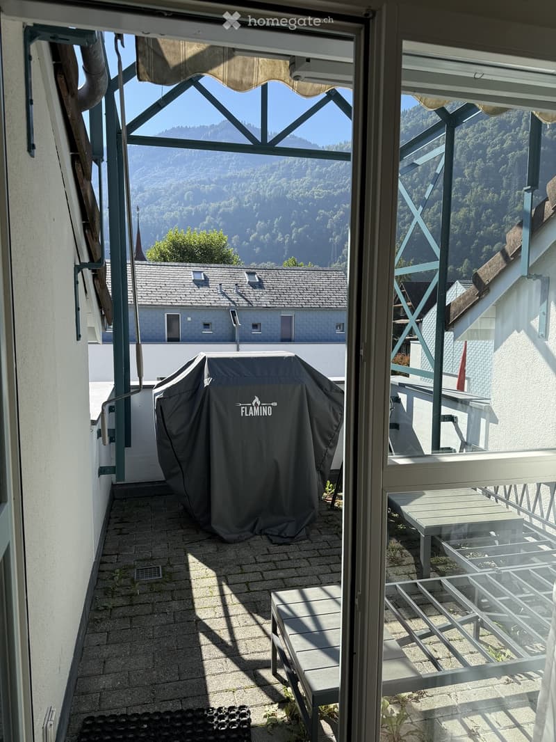 Balcony with a covered grill, bench, and table, overlooking a scenic mountain view.