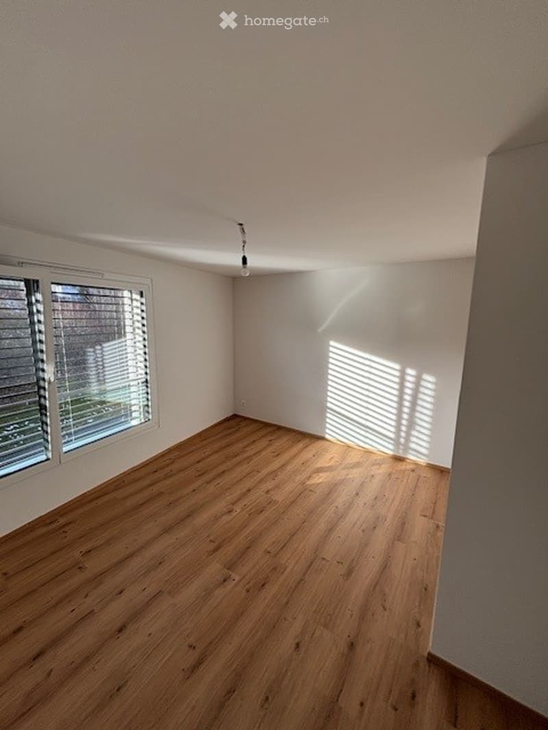 Empty room with wooden flooring, white walls, and large windows with blinds. No furniture or equipment present.