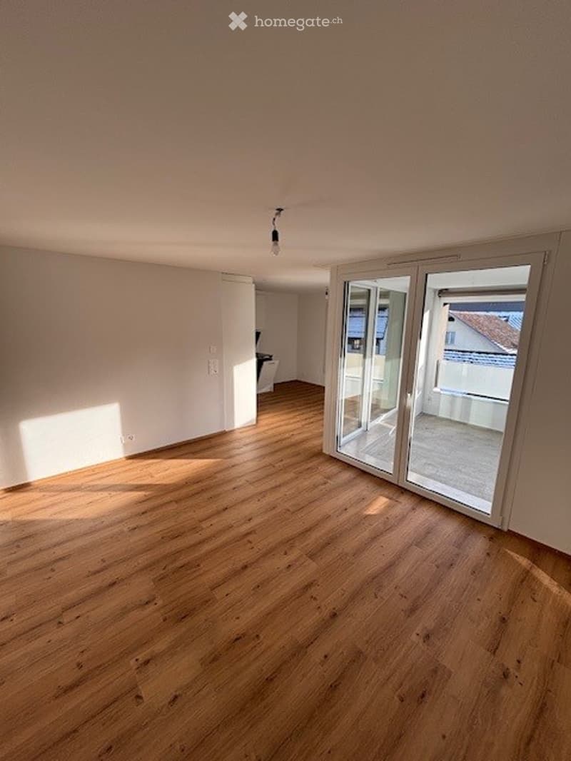 Empty room with wooden flooring, large sliding glass doors leading to a balcony, and white walls.