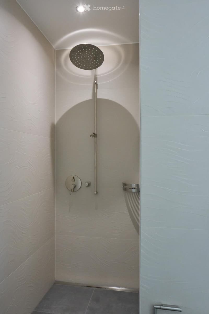 modern shower area with white tiled walls, shower head, and a metal shower rack