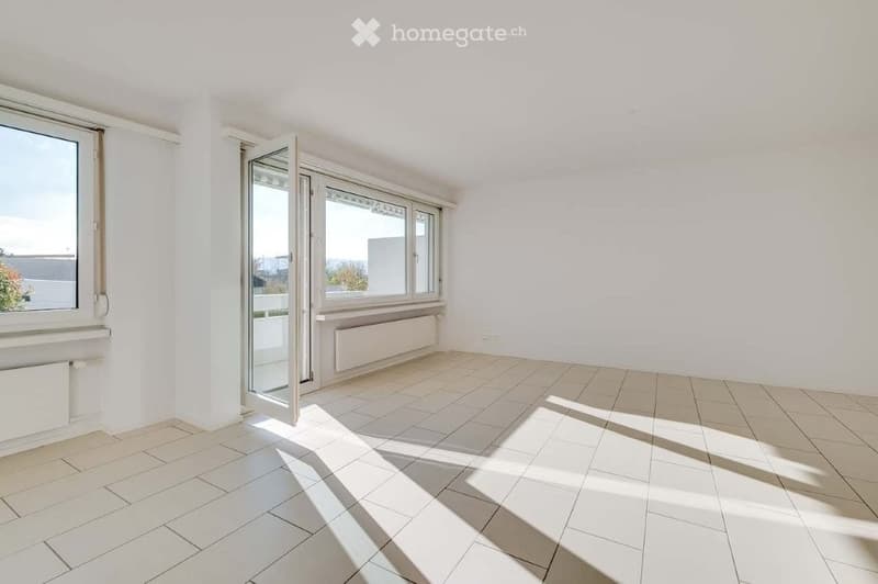 Empty room with white walls, tiled floor, large windows, and a sliding glass door leading to a balcony.