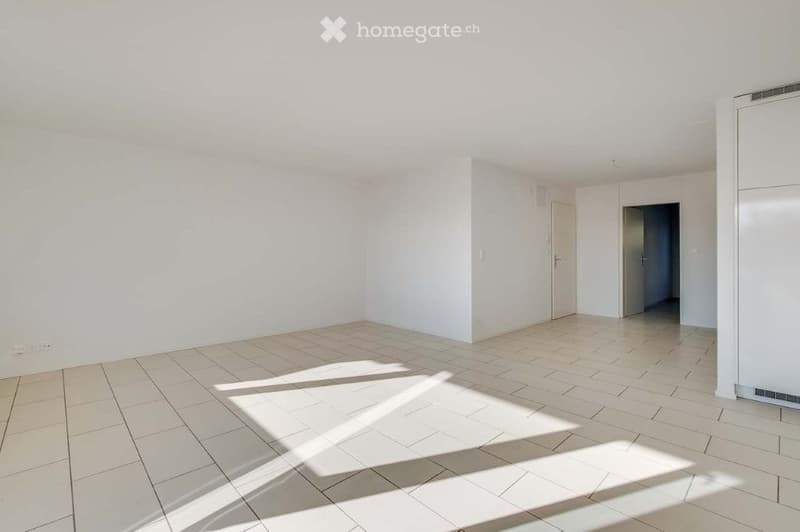 Empty room with white walls and tiled floor, featuring natural light from a window and a doorway leading to another space.