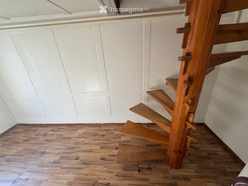 Wooden staircase with open design, white paneled walls, and wooden flooring in a narrow hallway.