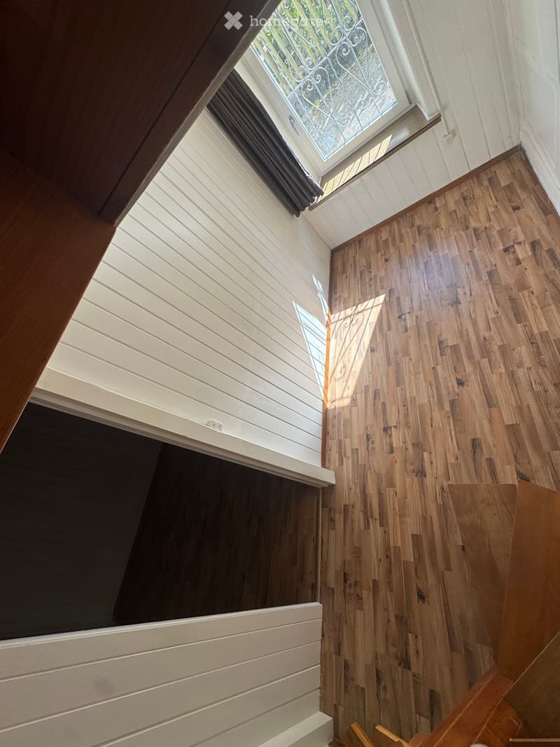 Staircase with wooden steps and white paneled walls, featuring a skylight window at the top.