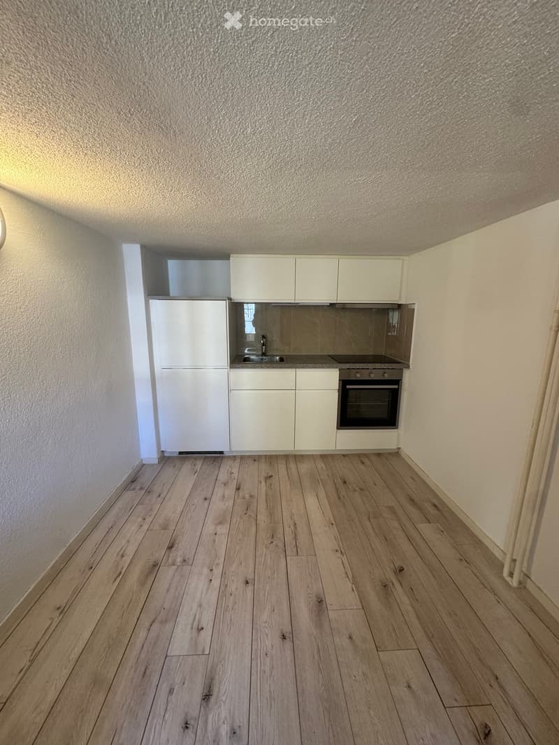 Empty kitchen with white cabinets, stainless steel sink, and oven, featuring light wooden flooring and white walls.