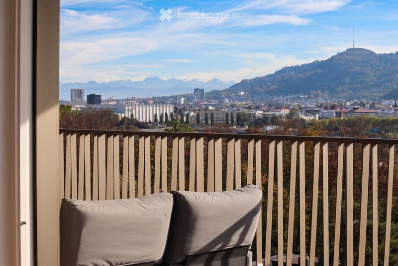 Balcony with a view of a cityscape and mountains, featuring a single chair with cushions.