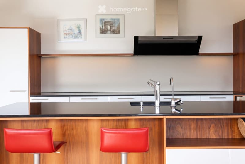 Modern kitchen with wooden cabinets, stainless steel faucet, and two red stools at the island.