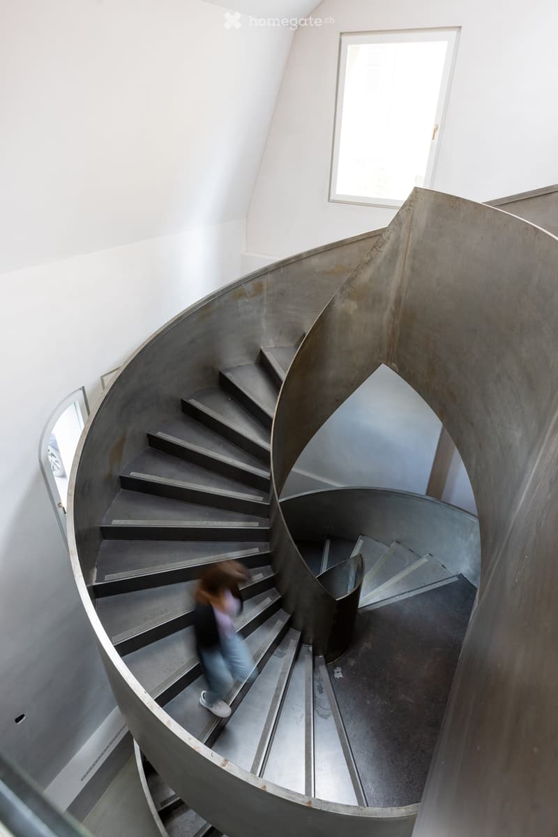 Spiral staircase with modern design, concrete steps, glass railing, and a person walking up the stairs.