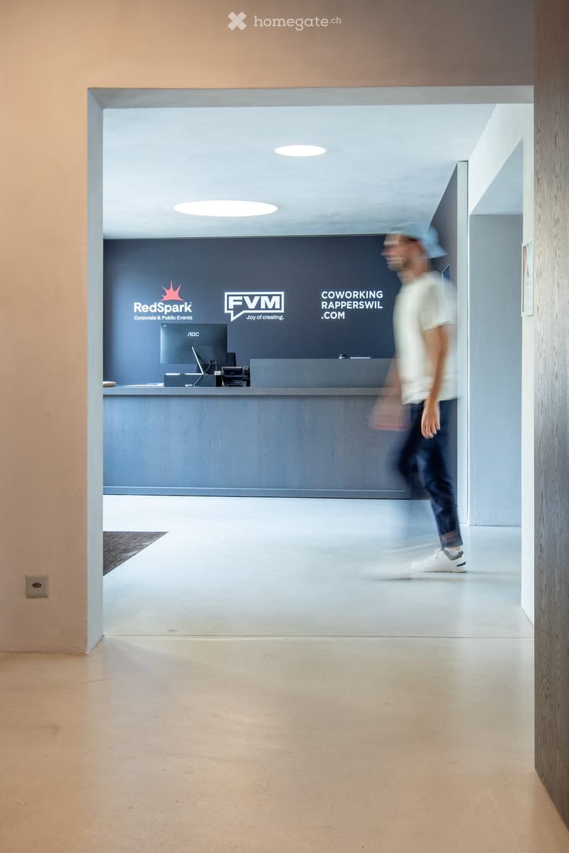 Modern hallway with a reception area featuring a counter, computer monitor, and signage for RedSpark and FVM. The space has light-colored walls, a polished concrete floor, and recessed ceiling lighting.