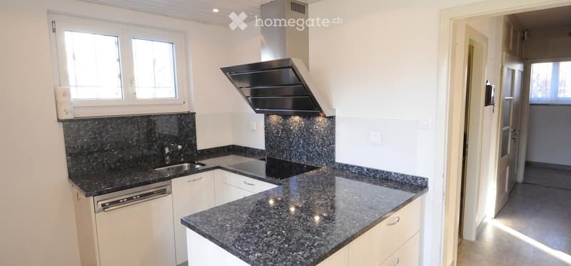Modern kitchen with granite countertops, white cabinets, stainless steel appliances, and a range hood.