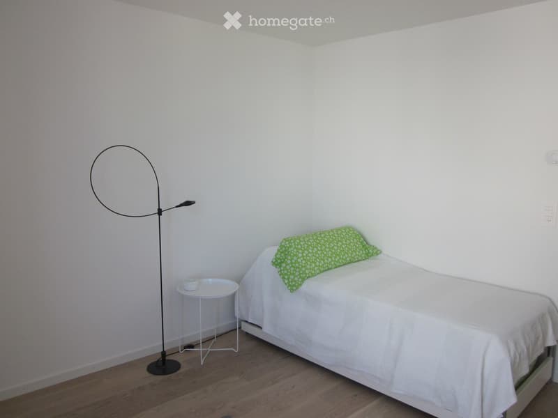 Minimalist bedroom with a single bed, white bedding, green pillow, small white nightstand, and a modern floor lamp.