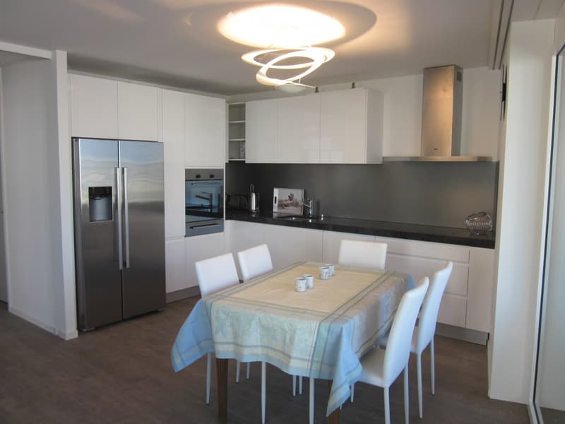 Modern kitchen with white cabinets, stainless steel appliances, a dining table with chairs, and a sleek pendant light fixture.