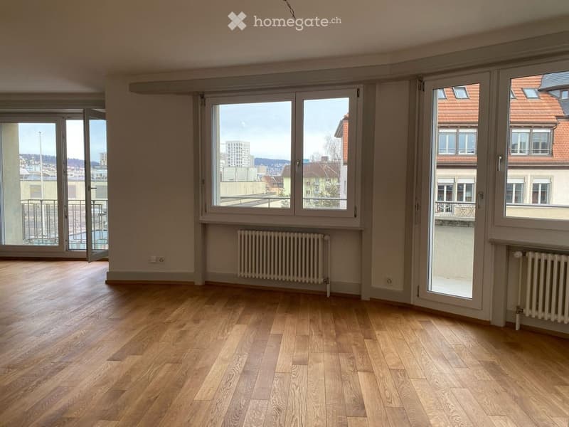 Empty room with wooden flooring, large windows, radiators, and a balcony door leading to a balcony.
