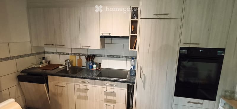 Modern kitchen with white cabinets, granite countertop, sink, oven, and dishwasher. Includes various kitchen utensils and appliances.