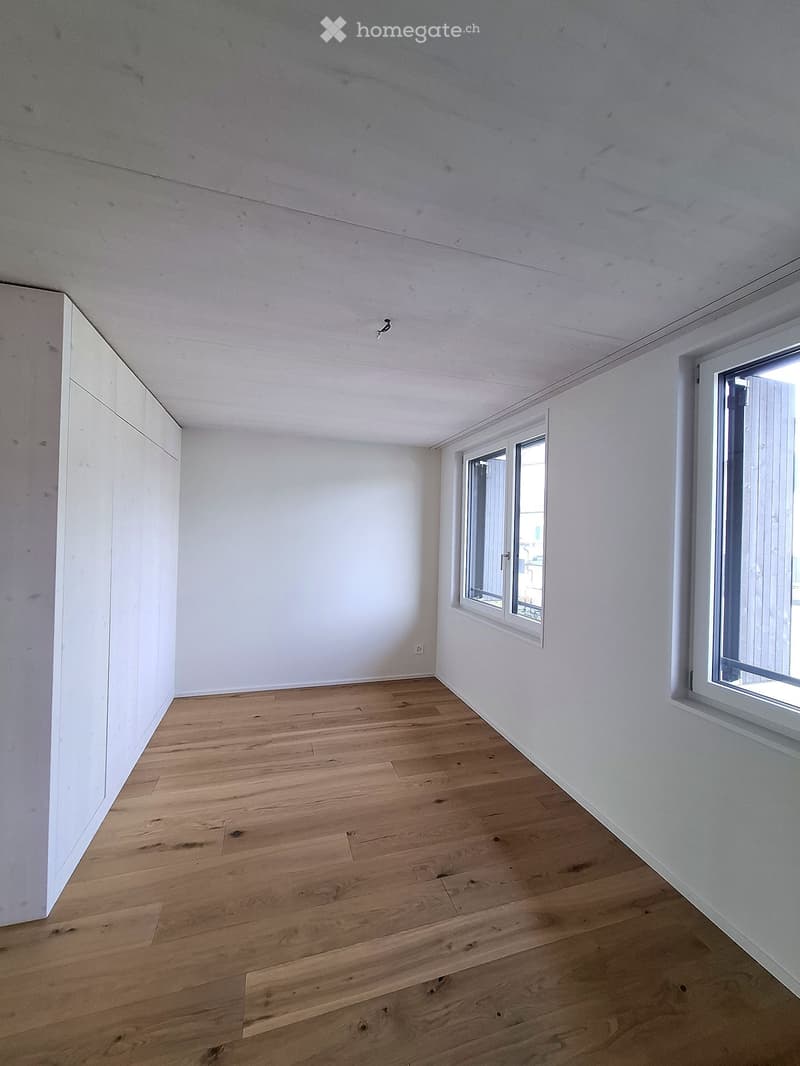 Empty room with light wooden flooring and white walls, featuring two windows and a built-in closet on one side.
