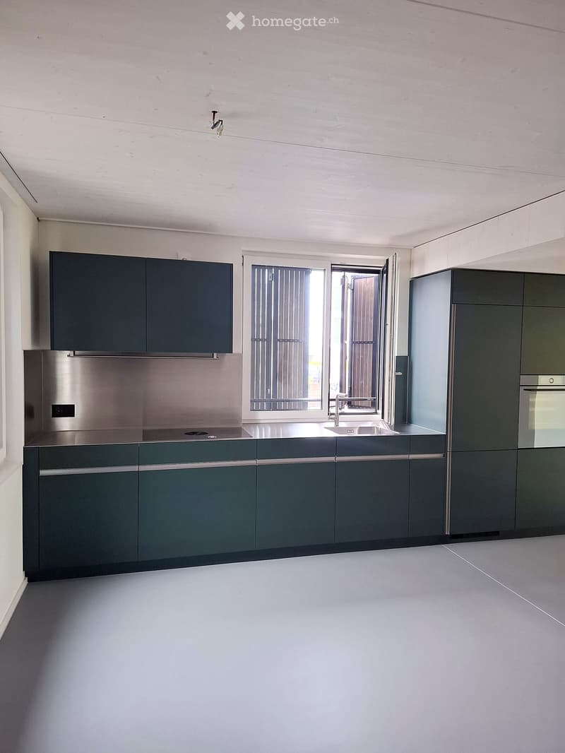 Modern kitchen with dark grey cabinets, stainless steel appliances, and a large window with blinds.
