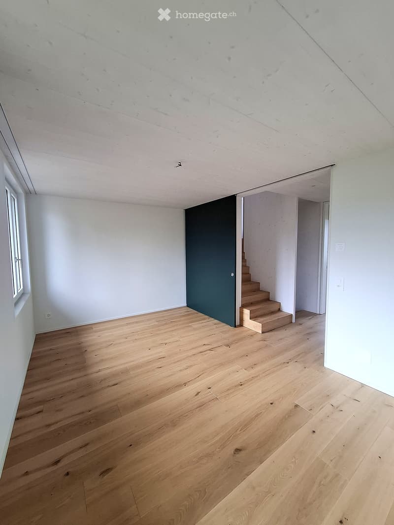 Empty room with light wooden flooring, white walls, and a staircase leading upwards.